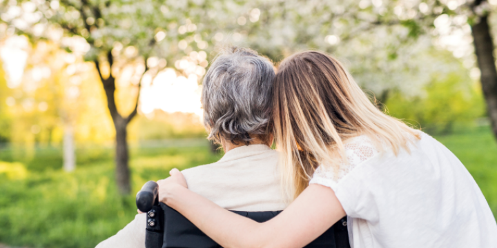 Eine blonde Frau umarmt eine ältere Person im Rollstuhl man sieht sie von hinten  &copy;Canva