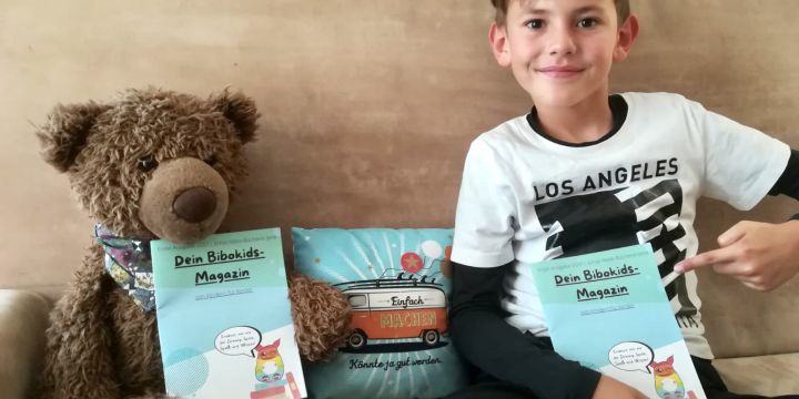 Ein Junge hält ein BibokidsMagazin der EAB in der Hand und neben ihm sitzt ein Plüschbär.  ©JenaKultur | EAB Jena 