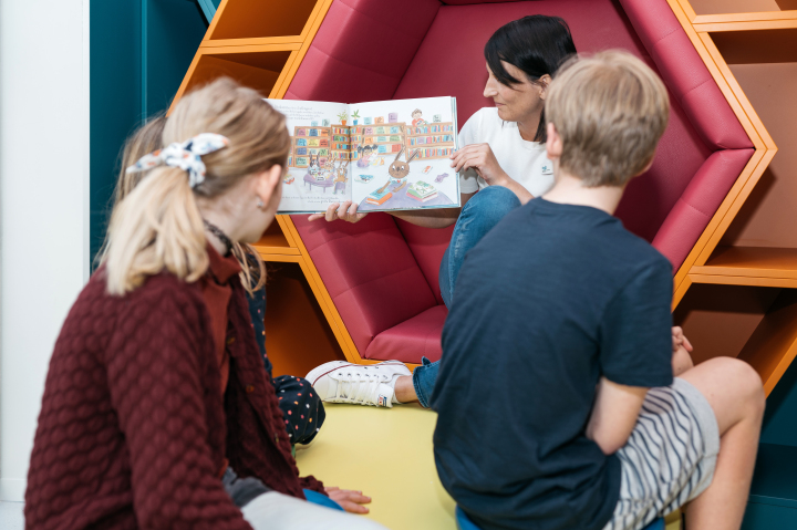 Frau ließtdrei Kindern ein Buch vor