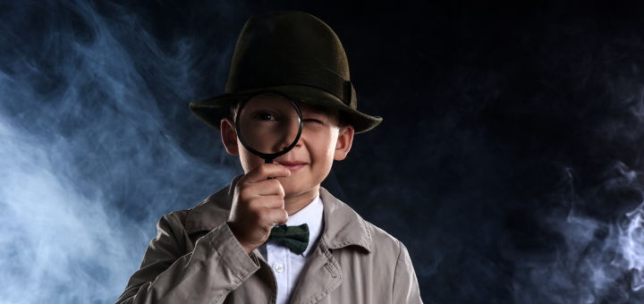 Ein Junge gekleidet wie ein Detektiv schaut durch eine Lupe